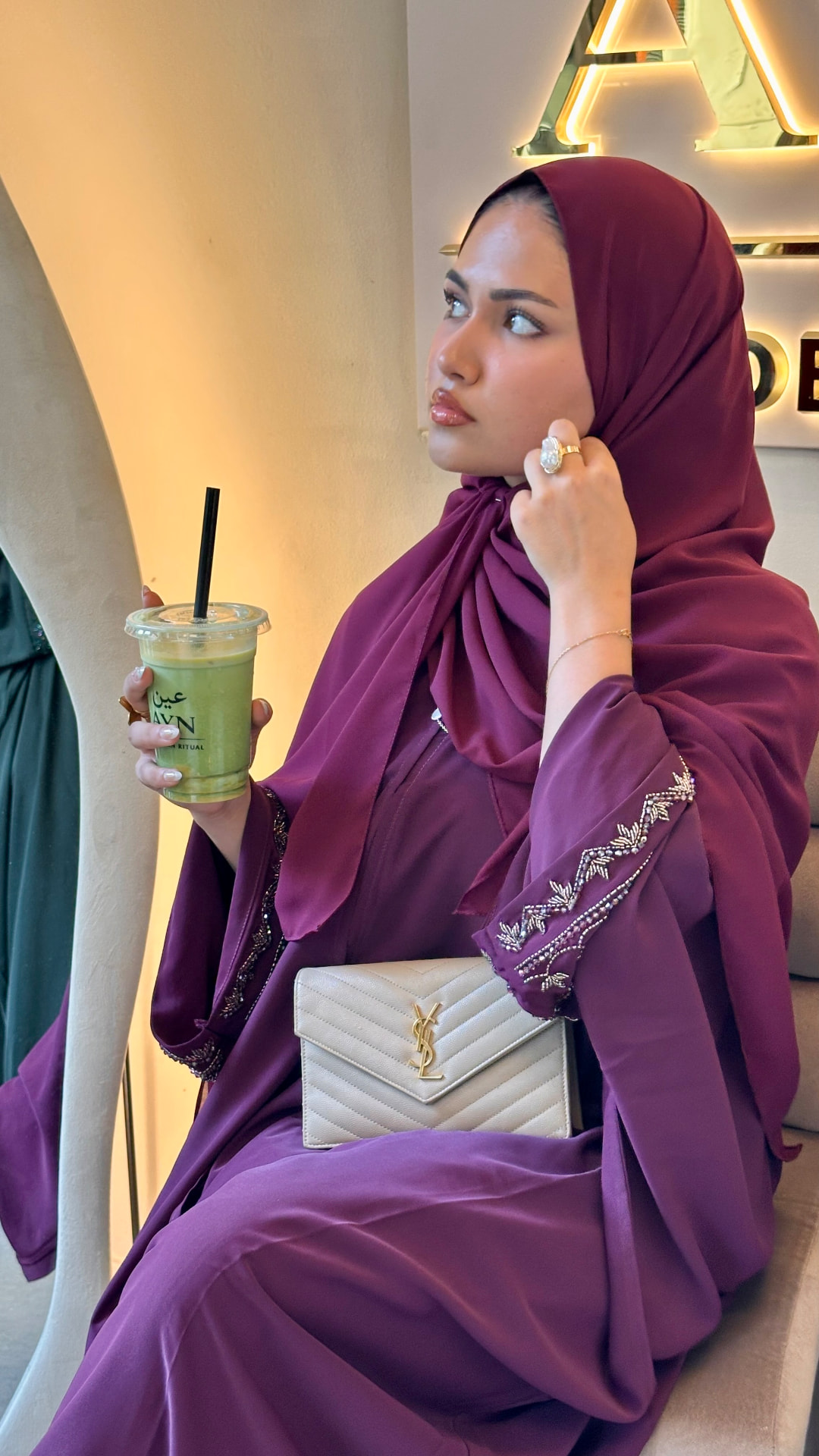 Azhara Abayas — model in a plum embellished abaya seated in a café.
