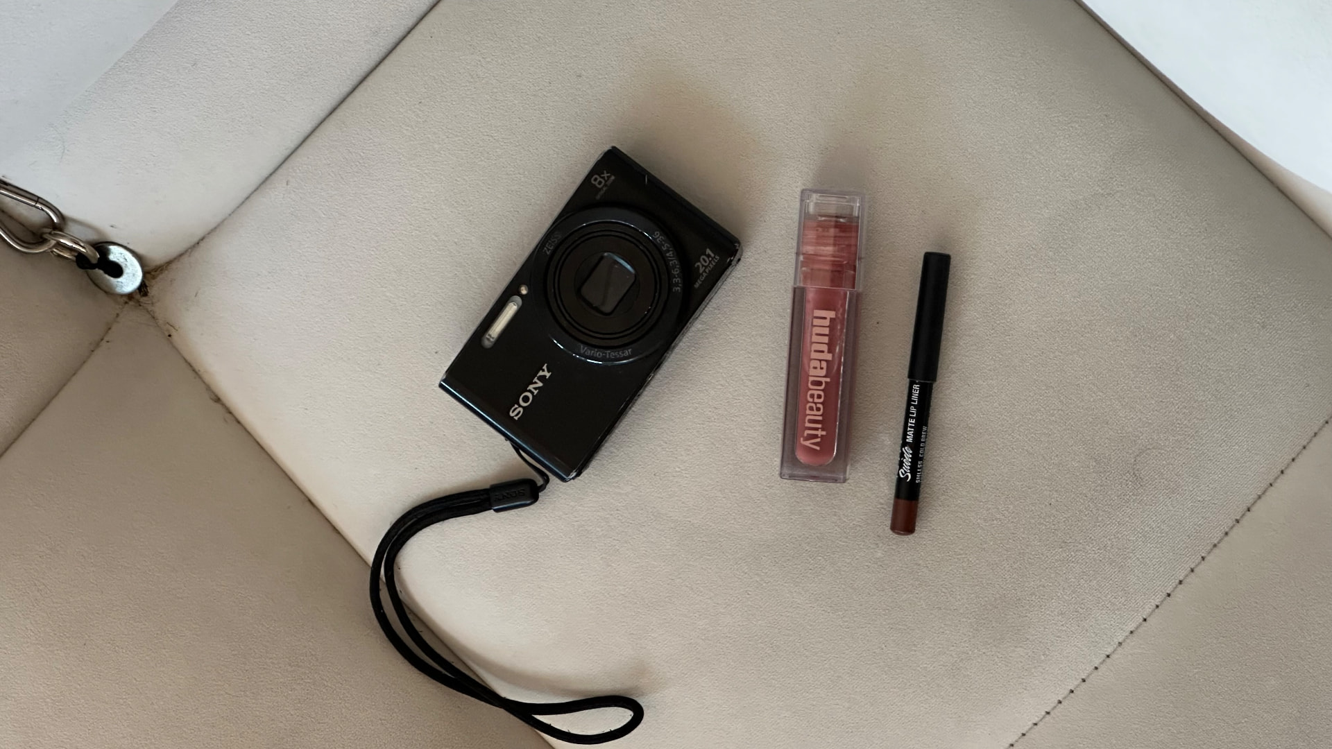 Sony compact camera beside lip gloss and lip liner on a cream sofa during a beauty shoot