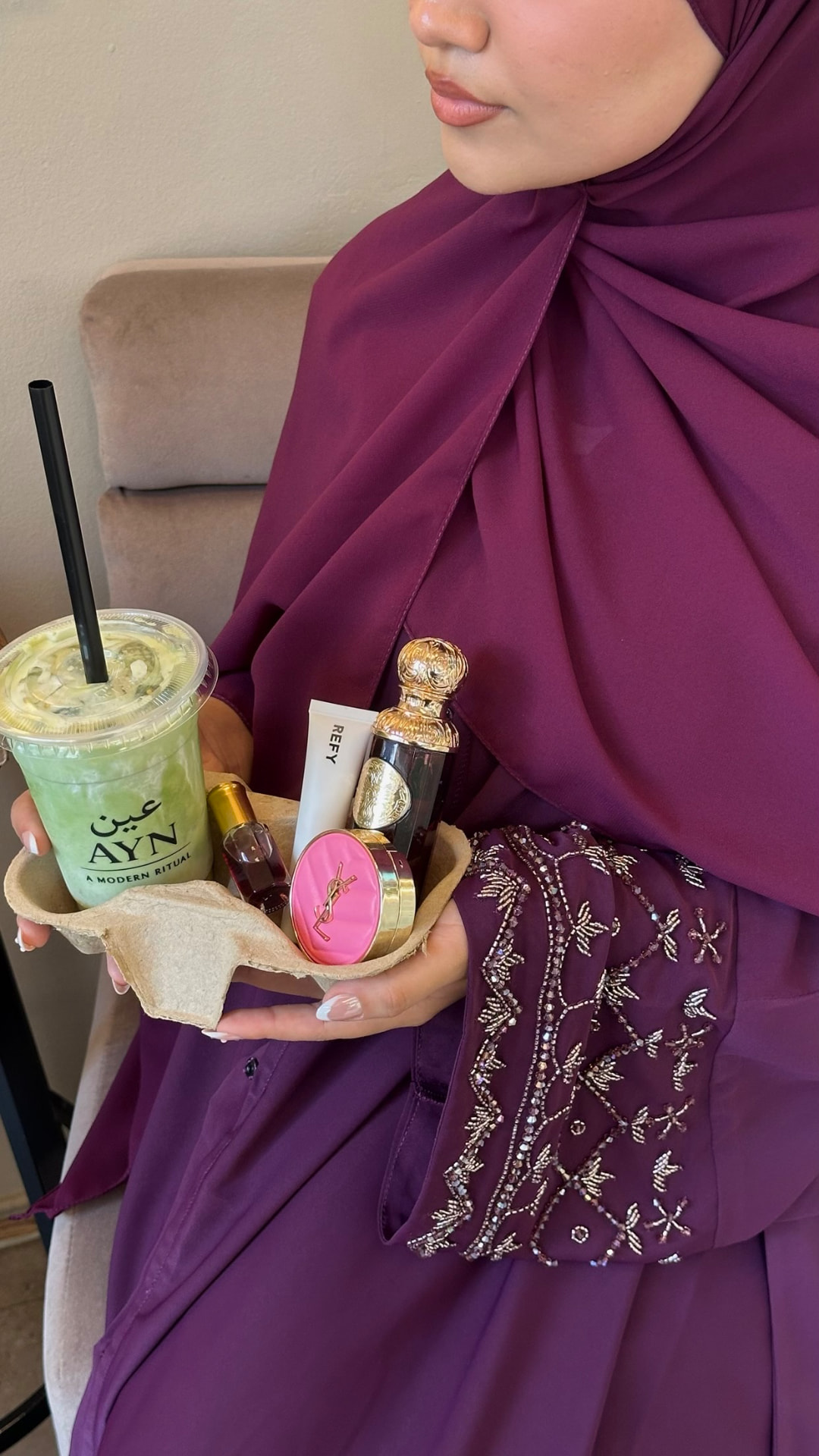 Azhara Abayas — styling detail of a plum abaya's beaded sleeve with beauty products.