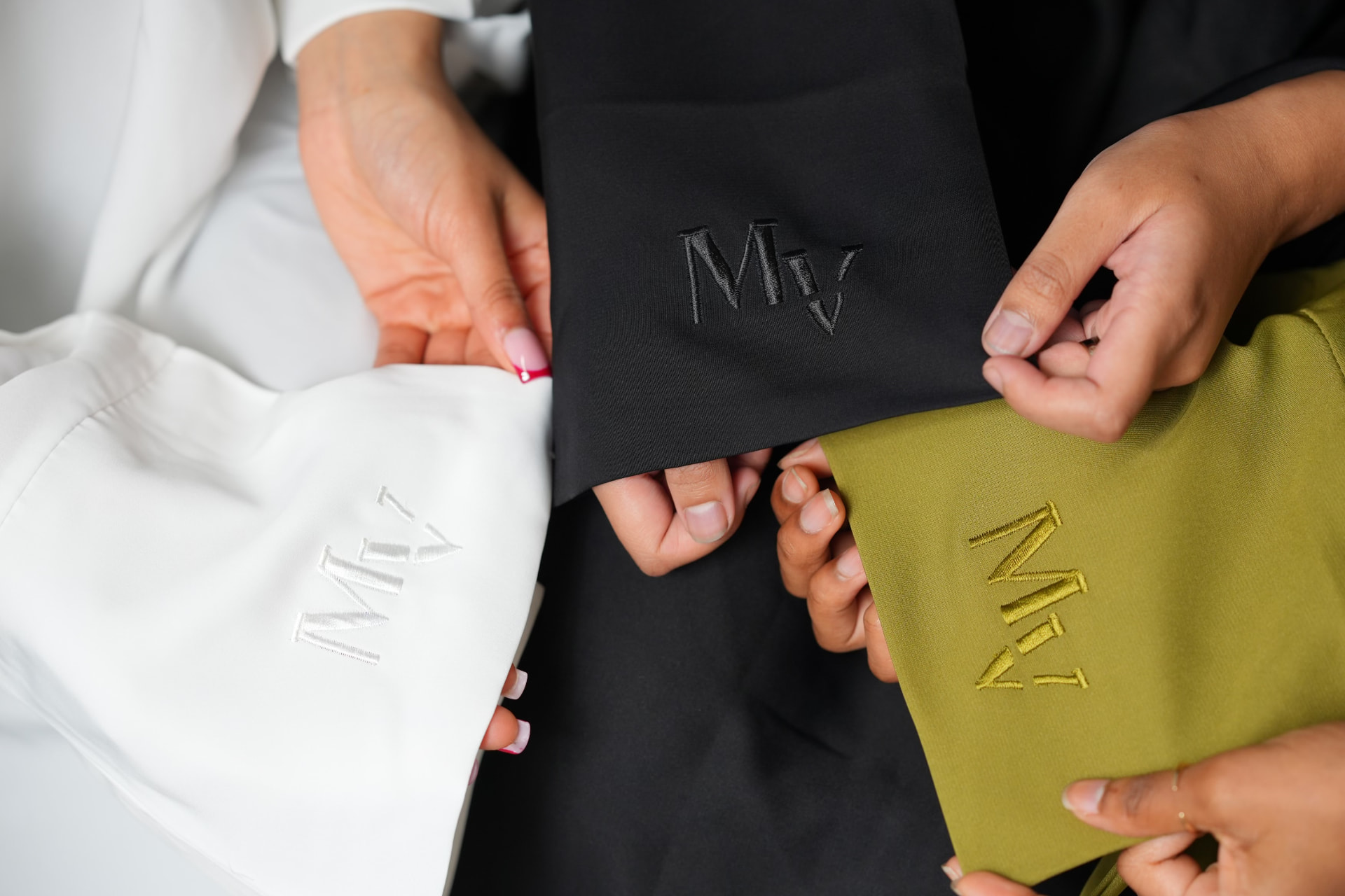 Close-up of MV monograms embroidered on white, black and olive fabric swatches.