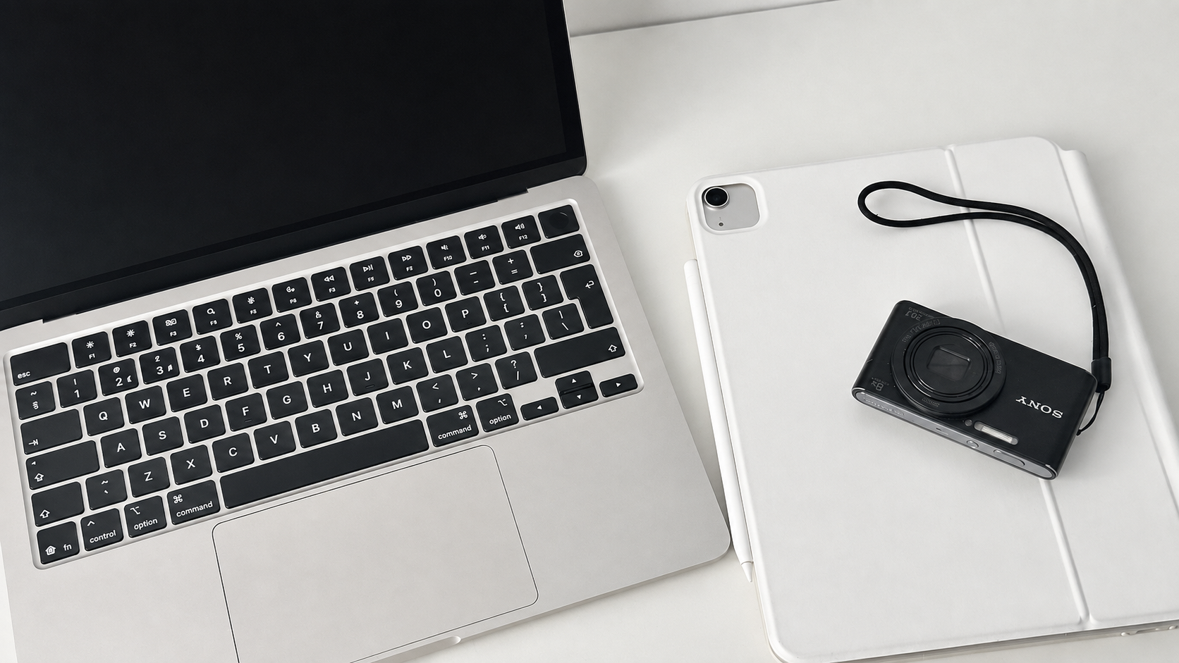 MacBook, iPad with stylus and a Sony compact camera arranged on a white desk