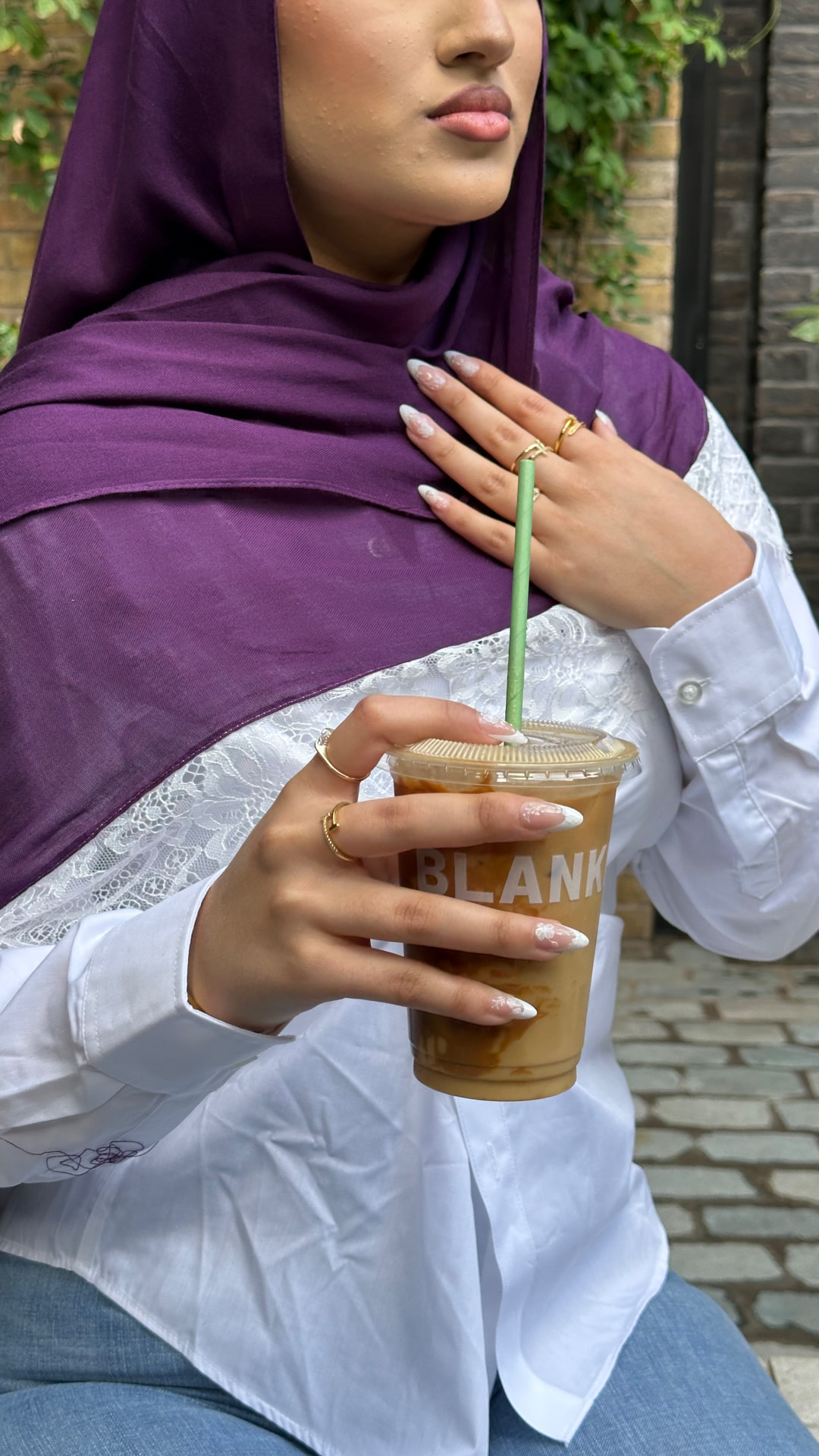 Detail shot of a model in a purple hijab holding an iced coffee.