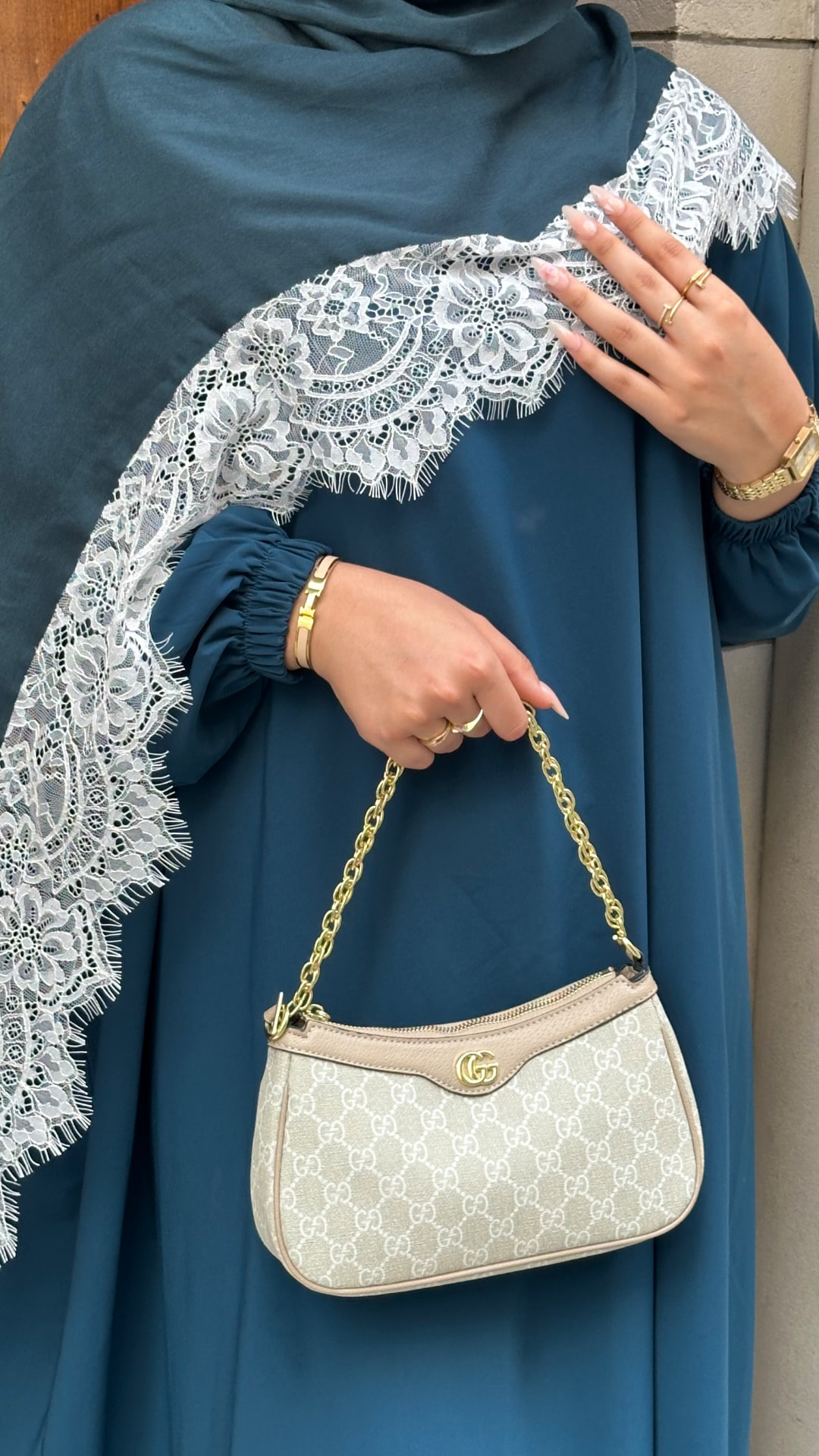 Close-up of a teal abaya sleeve and beige shoulder bag.